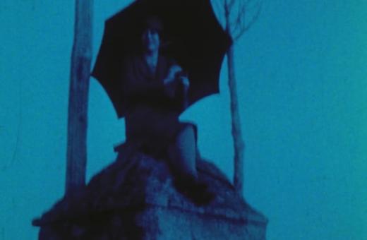 Still from the film, of a woman holding an umbrella atop a roof.