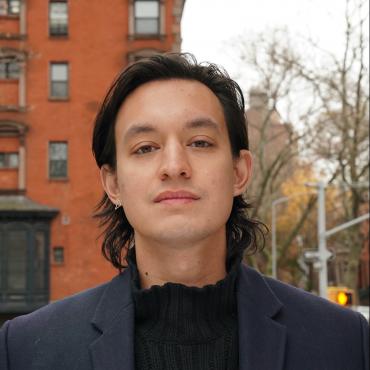 Headshot of Kyle Dacuyan in front of a red brick building and traffic lights