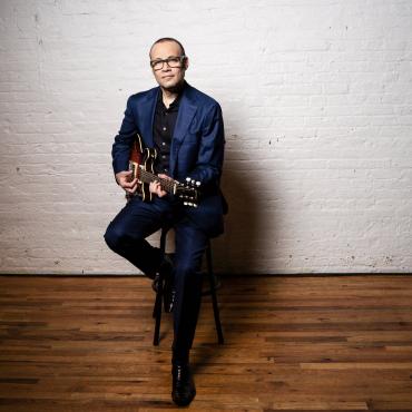 Liberty Ellman in a blue suit with his guitar.