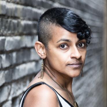 Chamindika Wanduragala, a forty-something Sri Lankan American puppet artist/stop motion filmmaker looking into the camera outside next to a building.