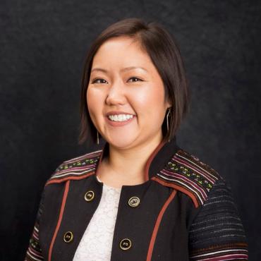 Joua Lee Grande, a Hmong-American woman wearing a blazer with Hmong designs sewn on the shoulders and arms smiling at the camera.