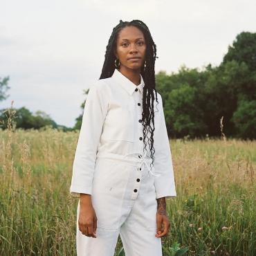 Nova Scott James, outside in a field with trees in the background, looking at the camera.