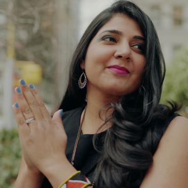 Portrait of a thirty-something Indian-American woman, with her palms touching, and her eyes looking to the side.