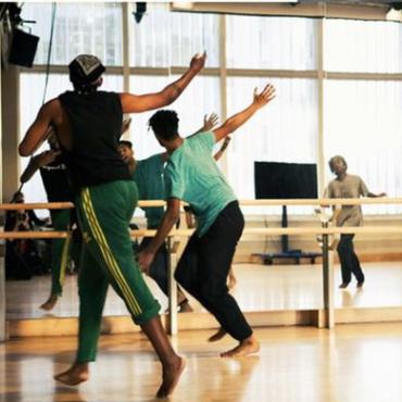 Four performers face a large dance mirror. Their arms extended in either direction. Their lilt falling to one side of the room. There is sweat, and smiles, and fatigue on their faces.