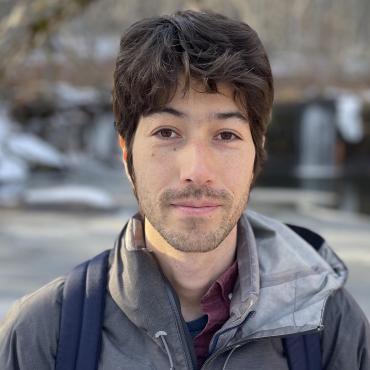 Gen Del Raye, a mixed-race writer, male, mid thirties, standing in front of a partially frozen river in Banning State Park, Minnesota.