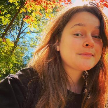 Halee Kirkwood, a 29 year-old Ojibwe and Swedish-American poet, smiles amongst autumn leaves on a trail at The Anderson Center in Red Wing, MN.