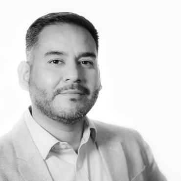 Rafael Samanez, a forty-something brown Latino man, wearing a white suit and looking confidently into the camera.