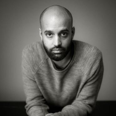 A black-and-white photo of a bald man with a beard looking directly into the camera.