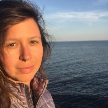 Maggie Thompson, a thirty two year old woman smiling at the camera in front of Lake Superior.