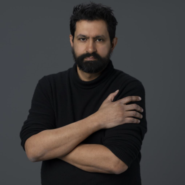 Sethi, wearing a black shirt and standing looking at the camera, with a gray backdrop behind him.