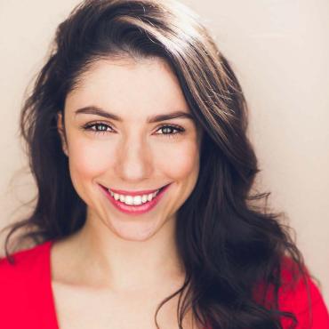 Dominique Nieves, a smiling Latina filmmaker with brown hair and a red dress.