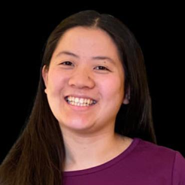 Medium close up photo of a smiling Chinese woman in her mid twenties with long black hair hiding most of a dark pink blazer and blue shirt.