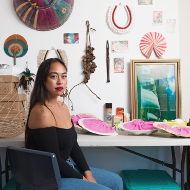 Caroline Garcia, a 30-something Filipina woman, sitting in front of her desk in her art studio, looking at the camera.