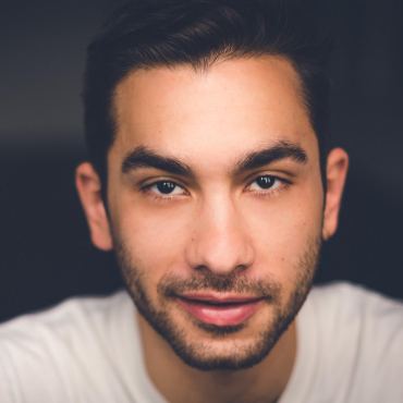 A light brown man looks at the camera with a mischievous kind of smile.