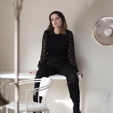 Lydia Cornett, a thirty-something white woman, sitting on a table and looking at the camera.