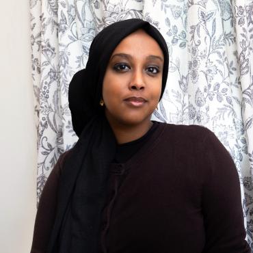 Yasmin, a Black woman wearing a headscarf and glasses, looking at the camera.