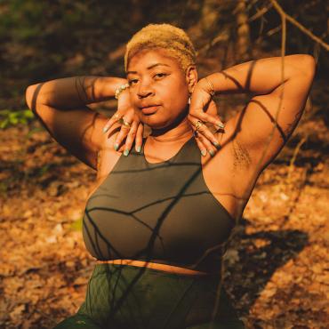 A forty something, Black woman in the woods under glowing sunlight.