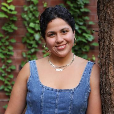 Ali smiling and leaning against a tree